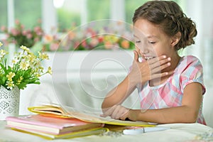 Little cute girl reading book at the table at home