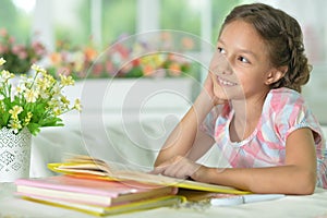 Little cute girl reading book at the table at home