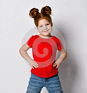 Little cute girl with red hair and freckles holds her hands at her waist and looks to the side.