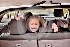 Little cute girl with red hair smiling at the background of the car interior