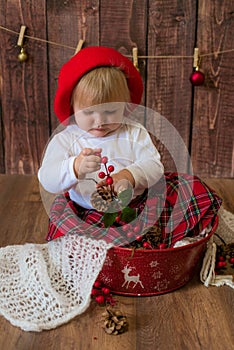 A little cute girl in a red plaid skirt and a red felt beret plays with cones and Christmas toys in a room decorated for Christmas