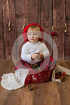 A little cute girl in a red plaid skirt and a red felt beret plays with cones and Christmas toys in a room decorated for Christmas