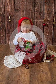 A little cute girl in a red plaid skirt and a red felt beret plays with cones and Christmas toys in a room decorated for Christmas