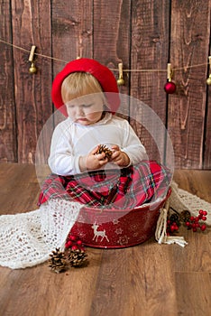 A little cute girl in a red plaid skirt and a red felt beret plays with cones and Christmas toys in a room decorated for Christmas