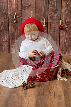 A little cute girl in a red plaid skirt and a red felt beret plays with cones and Christmas toys in a room decorated for Christmas