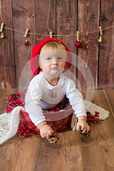 A little cute girl in a red plaid skirt and a red felt beret plays with cones and Christmas toys in a room decorated for Christmas