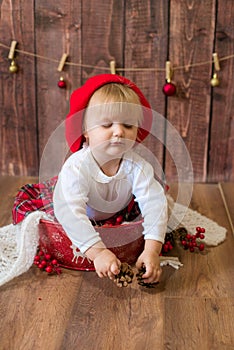 A little cute girl in a red plaid skirt and a red felt beret plays with cones and Christmas toys in a room decorated for Christmas