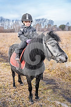 Little cute girl riding a little horse or pony in field in the winter