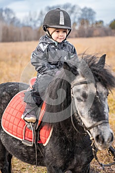 Little cute girl riding a little horse or pony in the winter in field in the winter