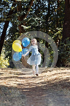 Little cute girl running in the Park with a bunch of balloons. She laughs provocatively. The concept of a happy childhood