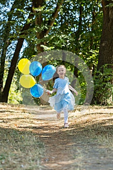 Little cute girl running in the Park with a bunch of balloons. She laughs provocatively. The concept of a happy childhood