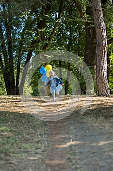 Little cute girl running in the Park with a bunch of balloons. She laughs provocatively. The concept of a happy childhood