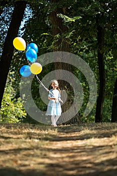 Little cute girl running in the Park with a bunch of balloons. She laughs provocatively. The concept of a happy childhood
