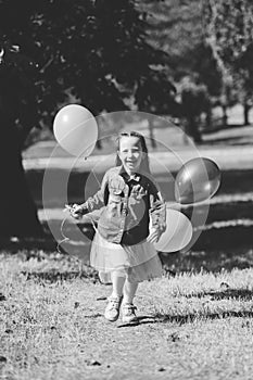 Little cute girl running in the Park with a bunch of balloons. She laughs provocatively. The concept of a happy childhood