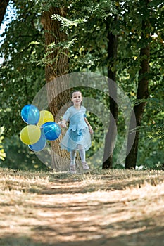 Little cute girl running in the Park with a bunch of balloons. She laughs provocatively. The concept of a happy childhood