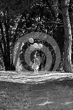 Little cute girl running in the Park with a bunch of balloons. She laughs provocatively. The concept of a happy childhood