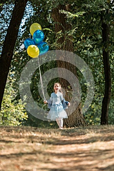 Little cute girl running in the Park with a bunch of balloons. She laughs provocatively. The concept of a happy childhood