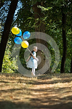 Little cute girl running in the Park with a bunch of balloons. She laughs provocatively. The concept of a happy childhood