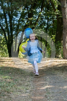 Little cute girl running in the Park with a bunch of balloons. She laughs provocatively. The concept of a happy childhood