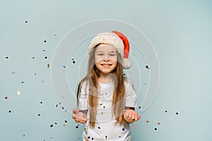 Little cute girl in santa hat throws up confetti and looks at the camera. christmas party