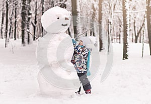 Little cute girl sculpts a big snowman in winter in the park