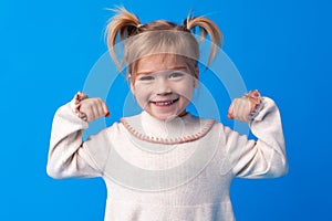 Little cute girl showing her strength against blue background