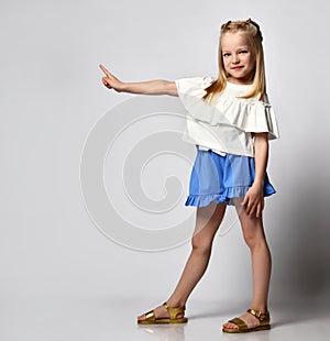 Little cute girl shows a finger to the side while standing on a white background.