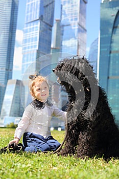 Little cute girl sits on grass with big black dog