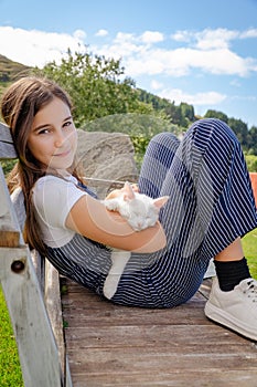 Little cute girl sits outdoors on sunny day and holds white cat in her arms