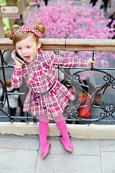 Little cute girl stands near wrought railings and shouts to mobile