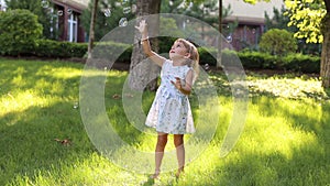 A little cute girl in a summer light dress playing with soap bubbles in the Park