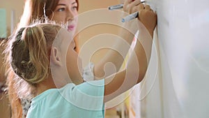 Little cute girl with teacher writing on the blackboard in classroom