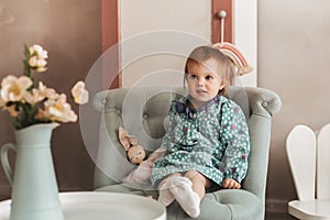 Little cute girl Todler sits in a chair in a children`s room