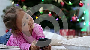 Little cute girl using smart phone, in front of Christmas tree. Close-up shot.