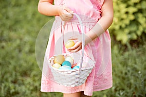 Little cute girl wear bunny ears holding basket with colorful painted eggs on Easter egg hunt in park