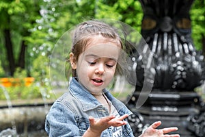 Little cute girl wets hands in the fountain