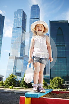 Little cute girl with white bag stands on sandbox