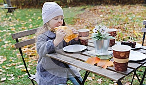 Little cute girls, sisters in coats seat, eat buns, drink coffee in cafe in autumn park. Cozy wooden table, chairs. Drinks,food to