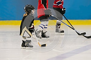 The little cute hockey girl is on the ice wearing in full equipment: hockey helmet, gloves, stick, skates. Figures of two teenager