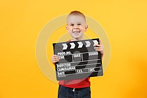 Little cute kid baby boy 3-4 years old in red t-shirt holding in hand classik black film making clapperboard looking