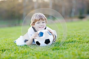 Little cute kid boy of 4 playing soccer with football on field, outdoors