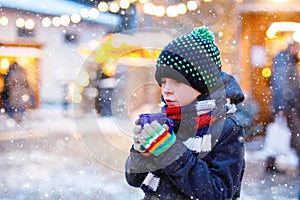 Little cute kid boy drinking hot children punch or chocolate on German Christmas market. Happy child on traditional