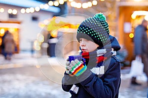 Little cute kid boy drinking hot children punch or chocolate on German Christmas market. Happy child on traditional