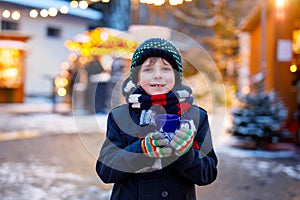 Little cute kid boy drinking hot children punch or chocolate on German Christmas market. Happy child on traditional