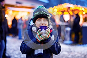 Little cute kid boy drinking hot children punch or chocolate on German Christmas market. Happy child on traditional