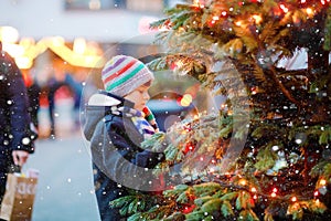 Little cute kid boy having fun on traditional Christmas market during strong snowfall. Happy child enjoying traditional