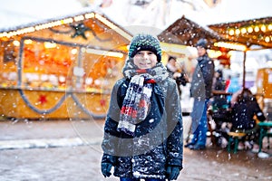 Little cute kid boy having fun on traditional German Christmas market during strong snowfall.. Happy child enjoying