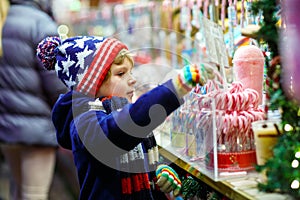 Little kid boy with candy cane stand on Christmas market