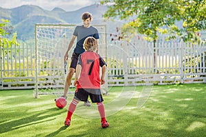 Little cute kid boy in red football uniform and his trainer or father playing soccer, football on field, outdoors