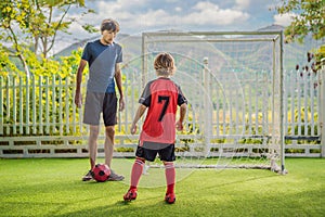 Little cute kid boy in red football uniform and his trainer or father playing soccer, football on field, outdoors